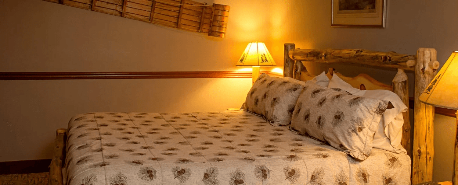 A cozy bedroom featuring a log-style bed with patterned bedding and warm lighting.