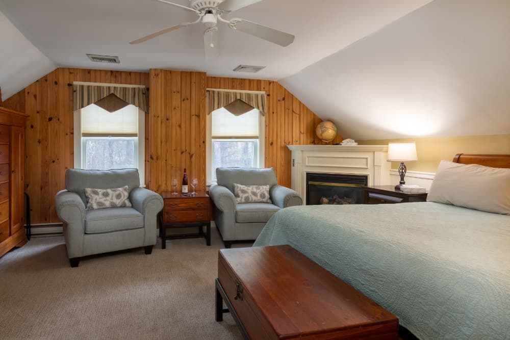 A cozy bedroom featuring a fireplace, two armchairs, and wooden accents.