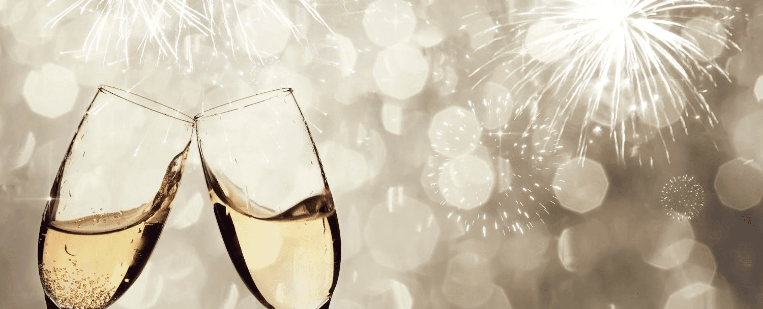 Two champagne glasses clink against a sparkling background with fireworks.