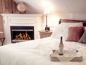 Cozy bedroom featuring a fireplace, a bottle of wine, and two glasses on a tray.