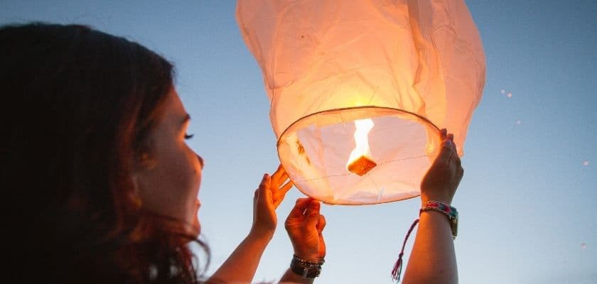 A person is holding a glowing sky lantern against a twilight sky.