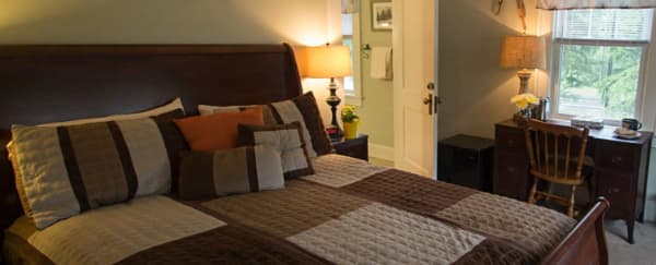 A cozy bedroom featuring a bed with patchwork bedding, a wooden desk, and a warm lamp.