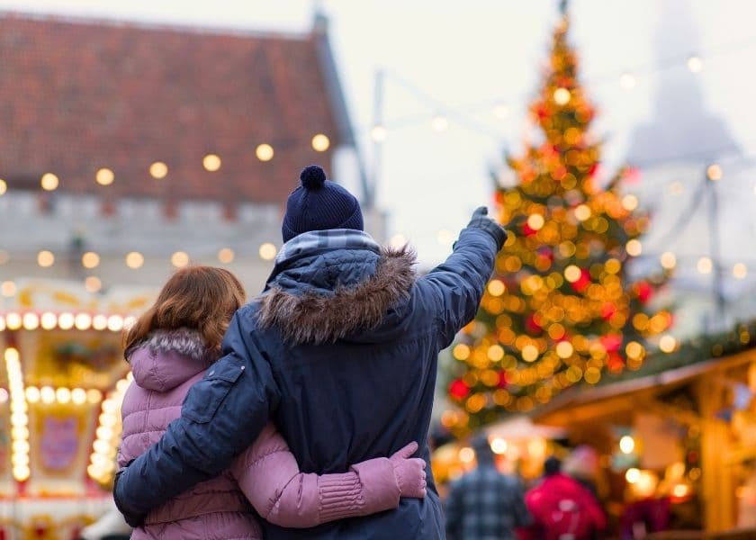 A couple embraces while admiring a Christmas tree in a festive market. A couple embraces while admiring a Christmas tree in a festive market.