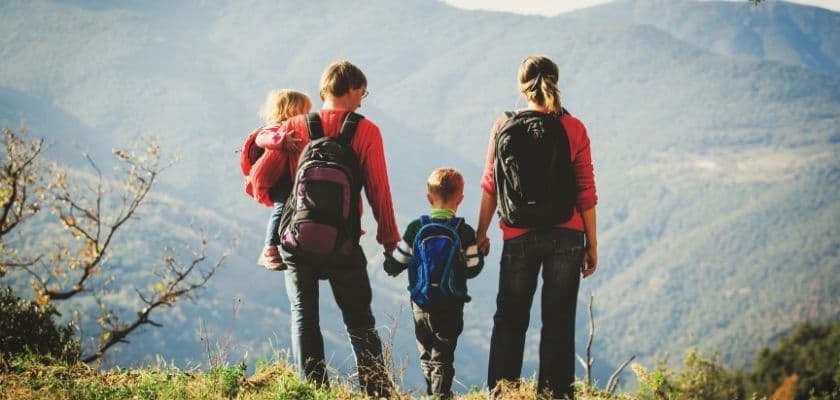 family hiking on a mountain overlook with backpacks and a child on one parents back