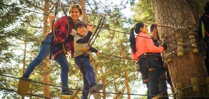 A woman and child smiling while crossing a treetop rope course in a forest