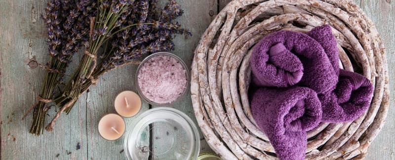 A basket of purple towels, along with a bunch of fresh lavender, candles, and bath salts